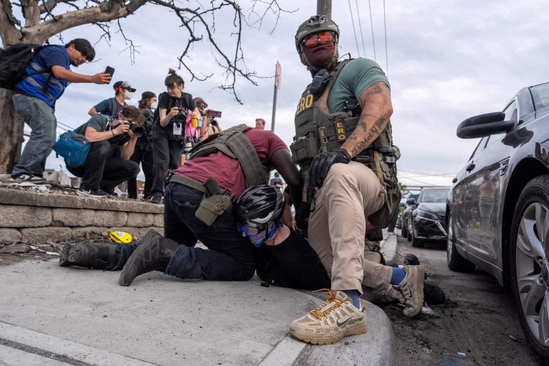 ICE agents in tactical gear restraining a protester on the ground outside a detention facility at night
