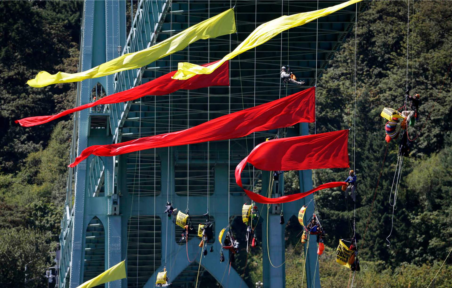 Activists dangle from ropes strung with red and yellow banners beneath the St. Johns Bridge, hovering over the river.