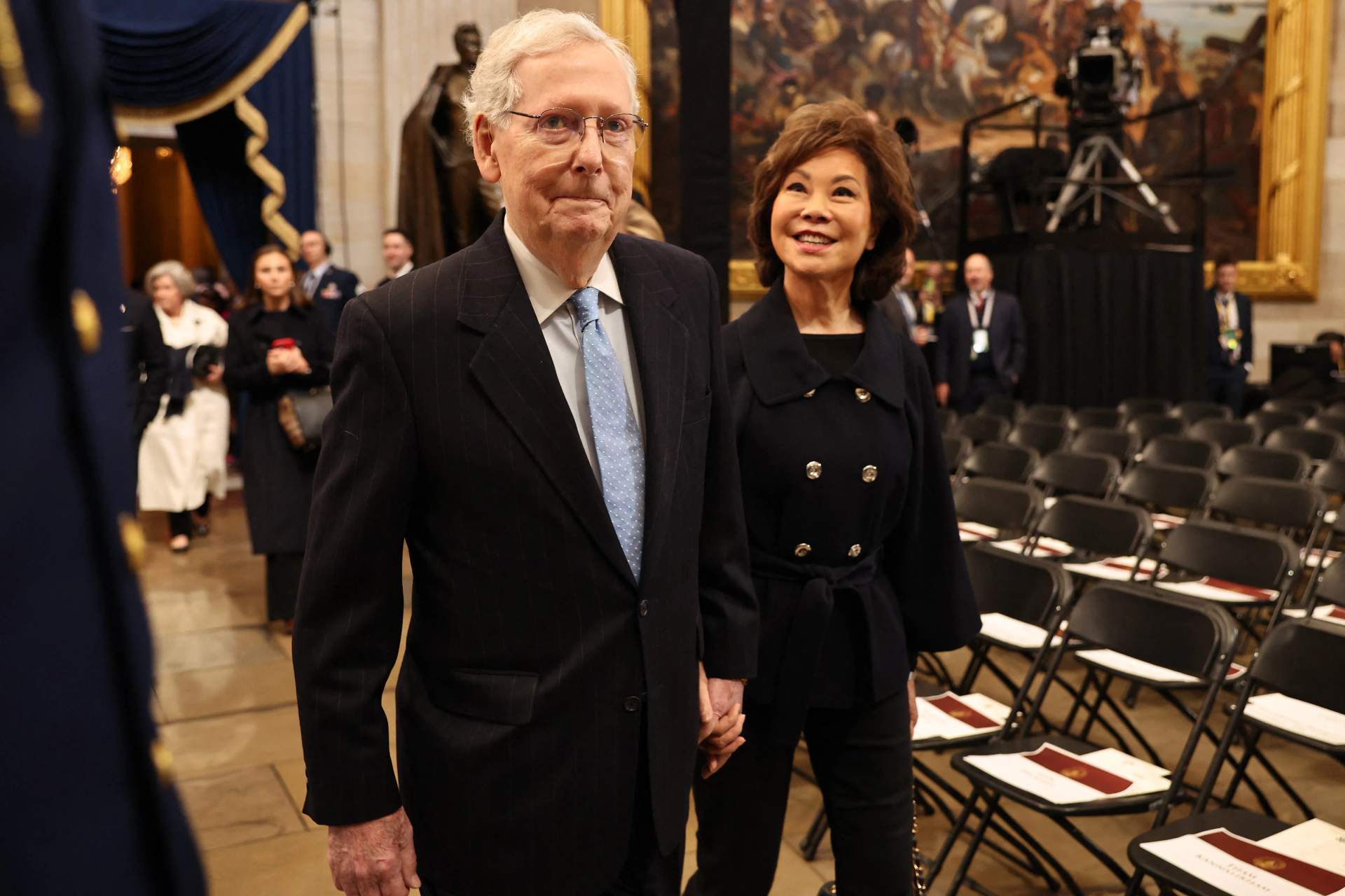 Mitch McConnell walking with his wife Elaine Chao, both dressed formally, at a public event
