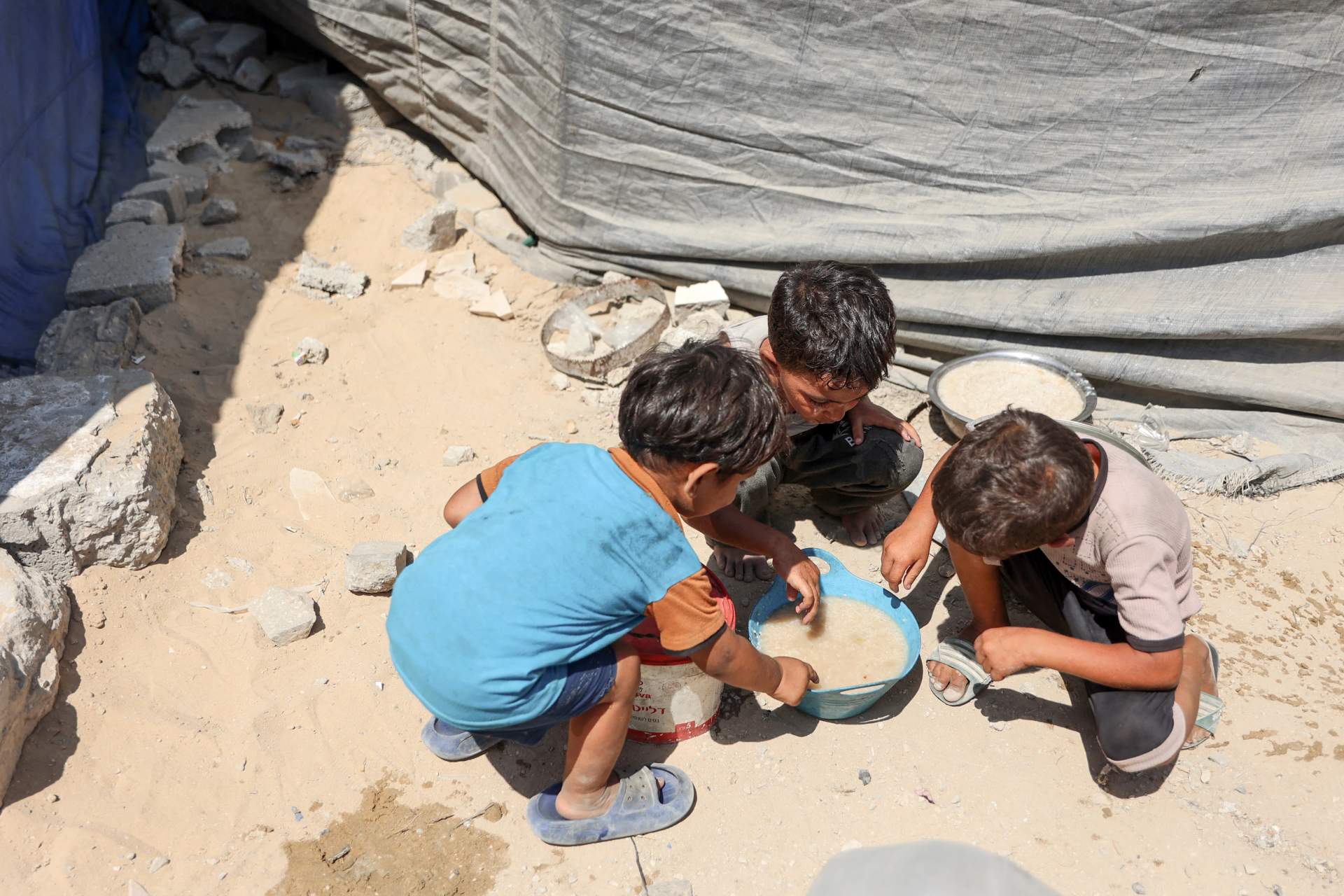 Palestinian children sharing a bowl of soup at a food distribution point in Gaza during famine