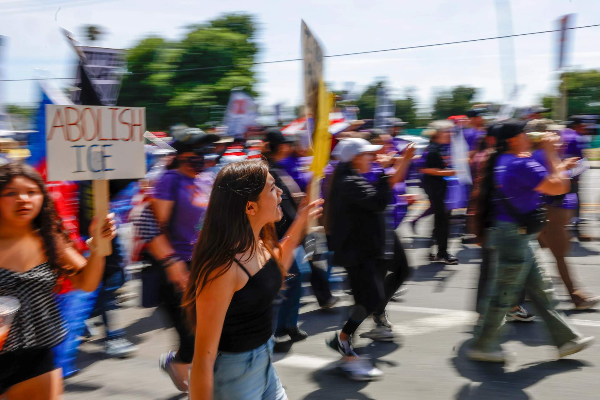 Large crowd of people marching down a city street during May Day 2026 protest with signs and banners visible