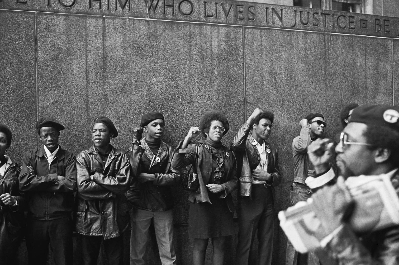 Young Black activist stand alongside wall with fist raised
