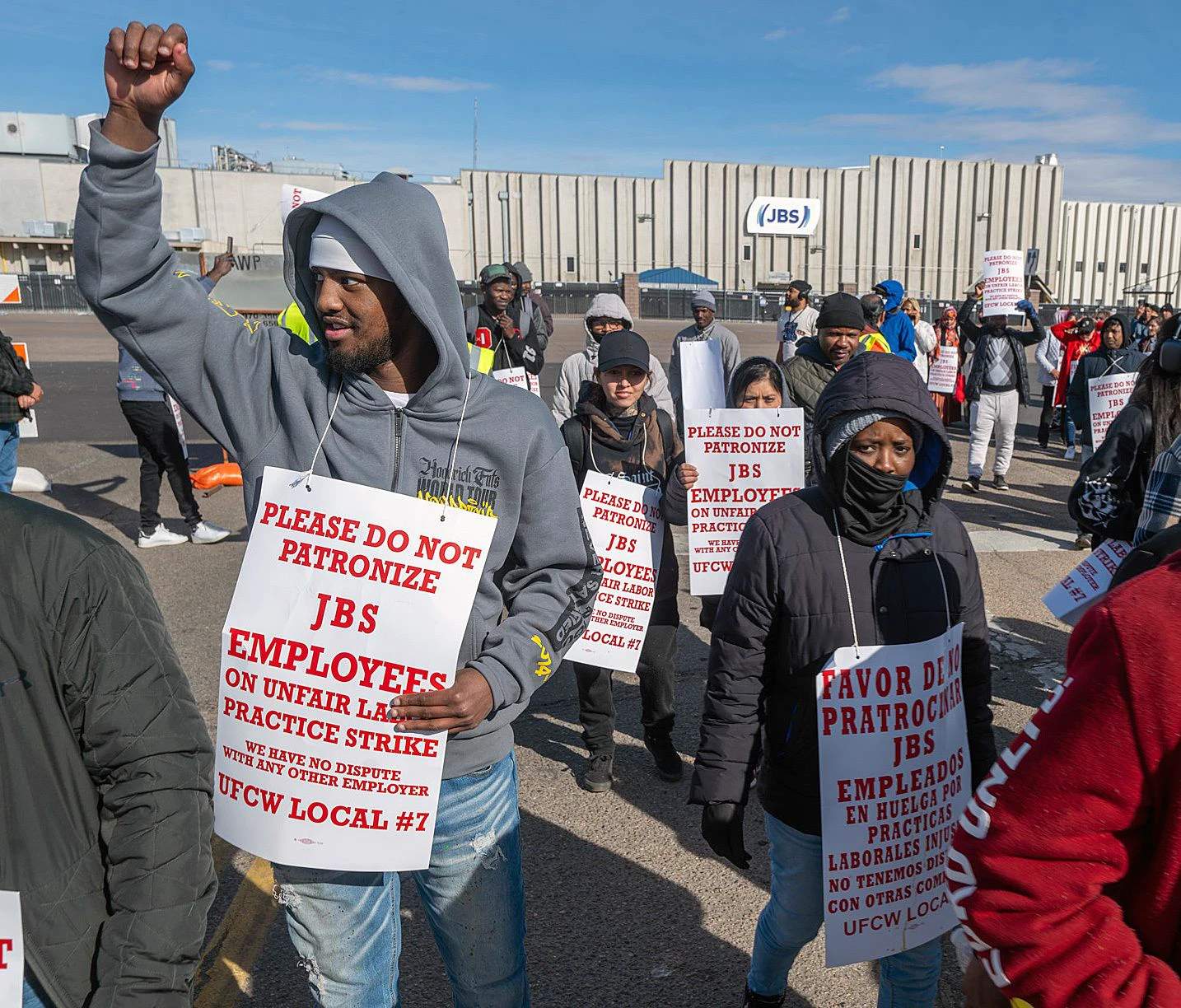 Group of striking meatpacking workers standing together holding protest signs outside the JBS plant