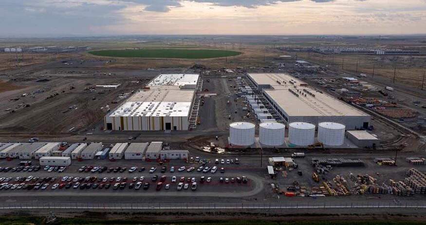 Amazon Web Services data center in Boardman, Oregon, with massive industrial buildings under construction against a cloudy sky