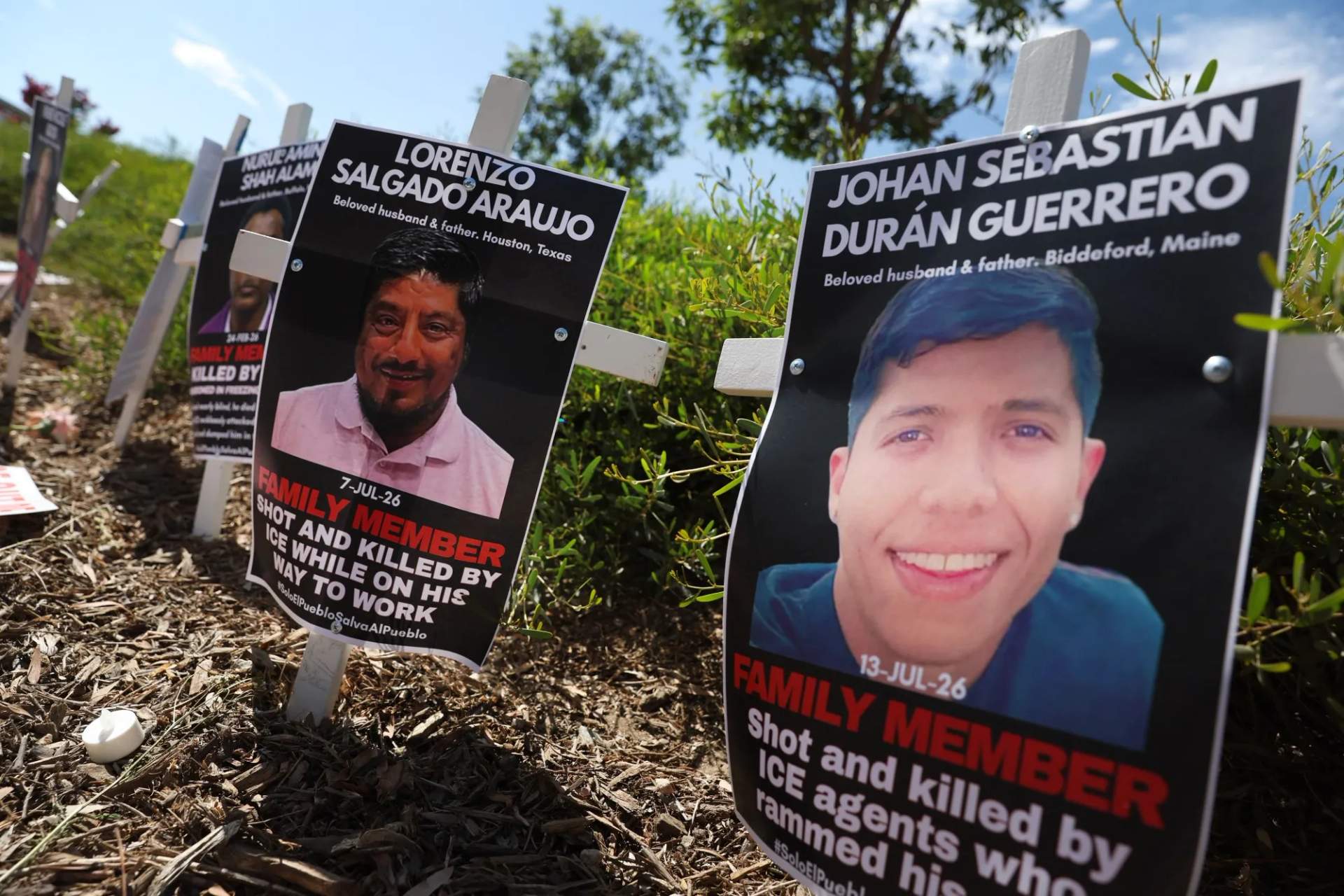 Rows of white crosses with photos attached planted in grass outside a Home Depot store during an ICE vigil