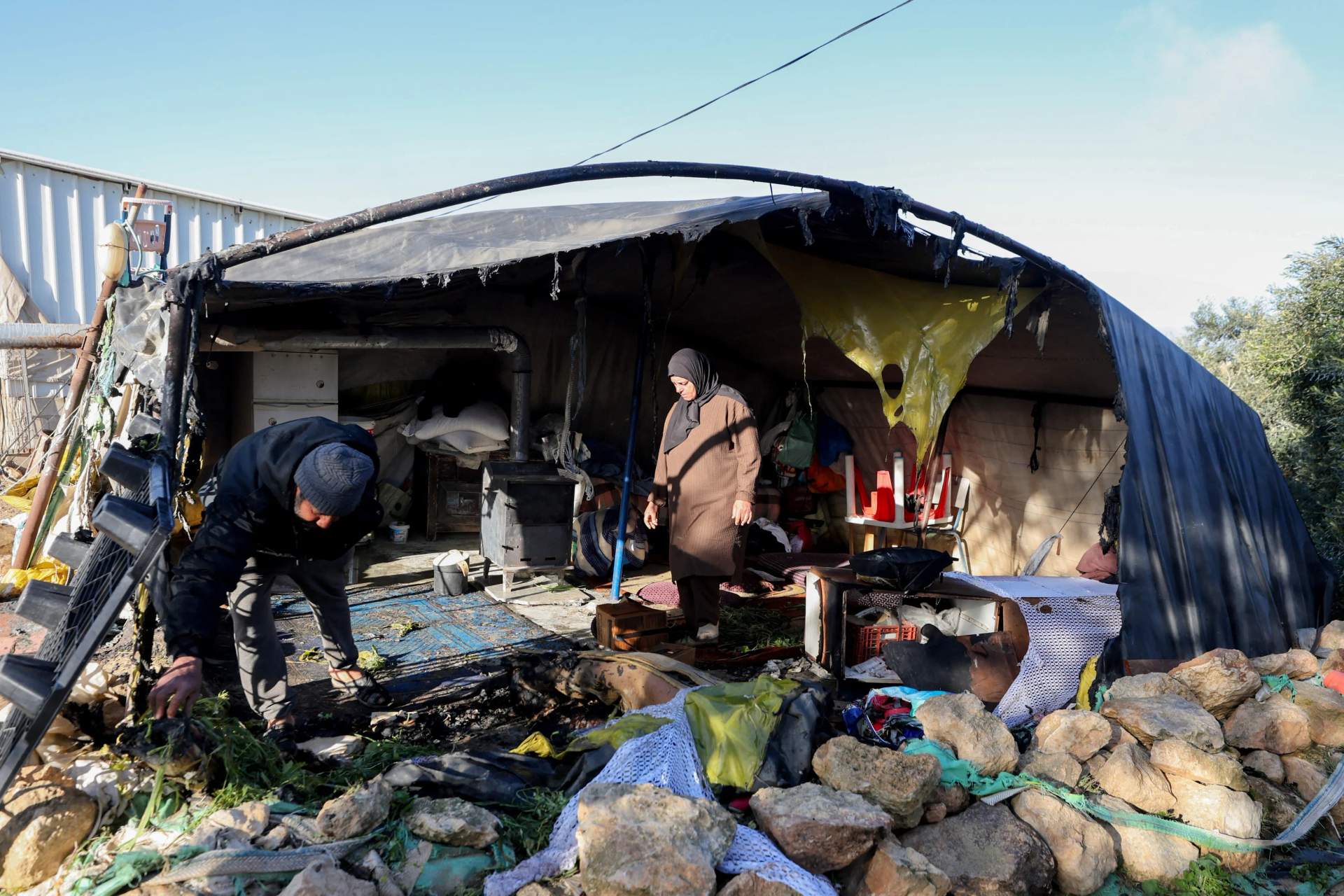 Palestinians stand inside a burned tent examining destroyed belongings after an Israeli settler attack in the village of Susya, Masafer Yatta, West Bank