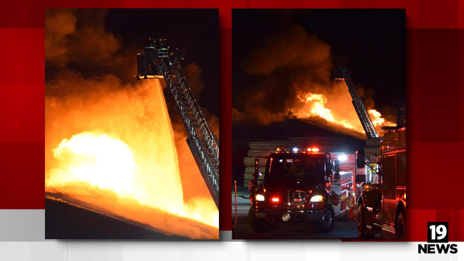 Nighttime photograph of a large lumber yard with stacked wooden pallets completely engulfed in intense orange flames, with fire hoses spraying water from multiple angles