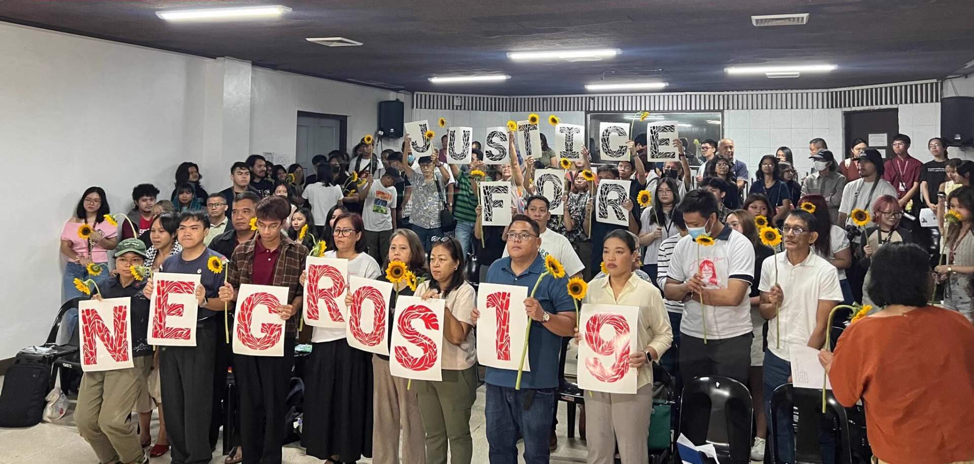 Large group of activists carrying banners and signs marching down a street during a Justice for Negros 19 protest rally