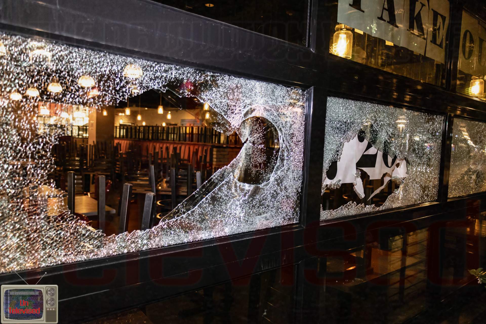 A restaurant's "Takeout" window area with a large jagged hole smashed through the glass, tables and string lights visible inside. [Radical Edward - Untelevised Media]