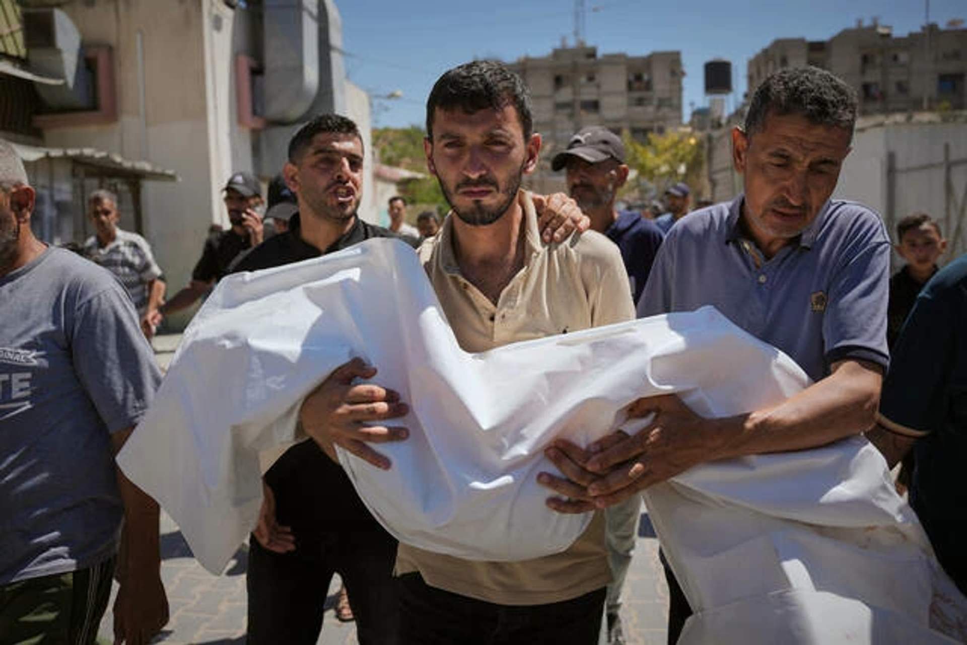 A Palestinian man carries the small shrouded body of a young girl through a hospital corridor during a funeral in Khan Younis