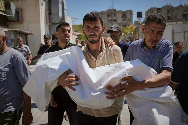 A Palestinian man carries the small shrouded body of a young girl through a hospital corridor during a funeral in Khan Younis