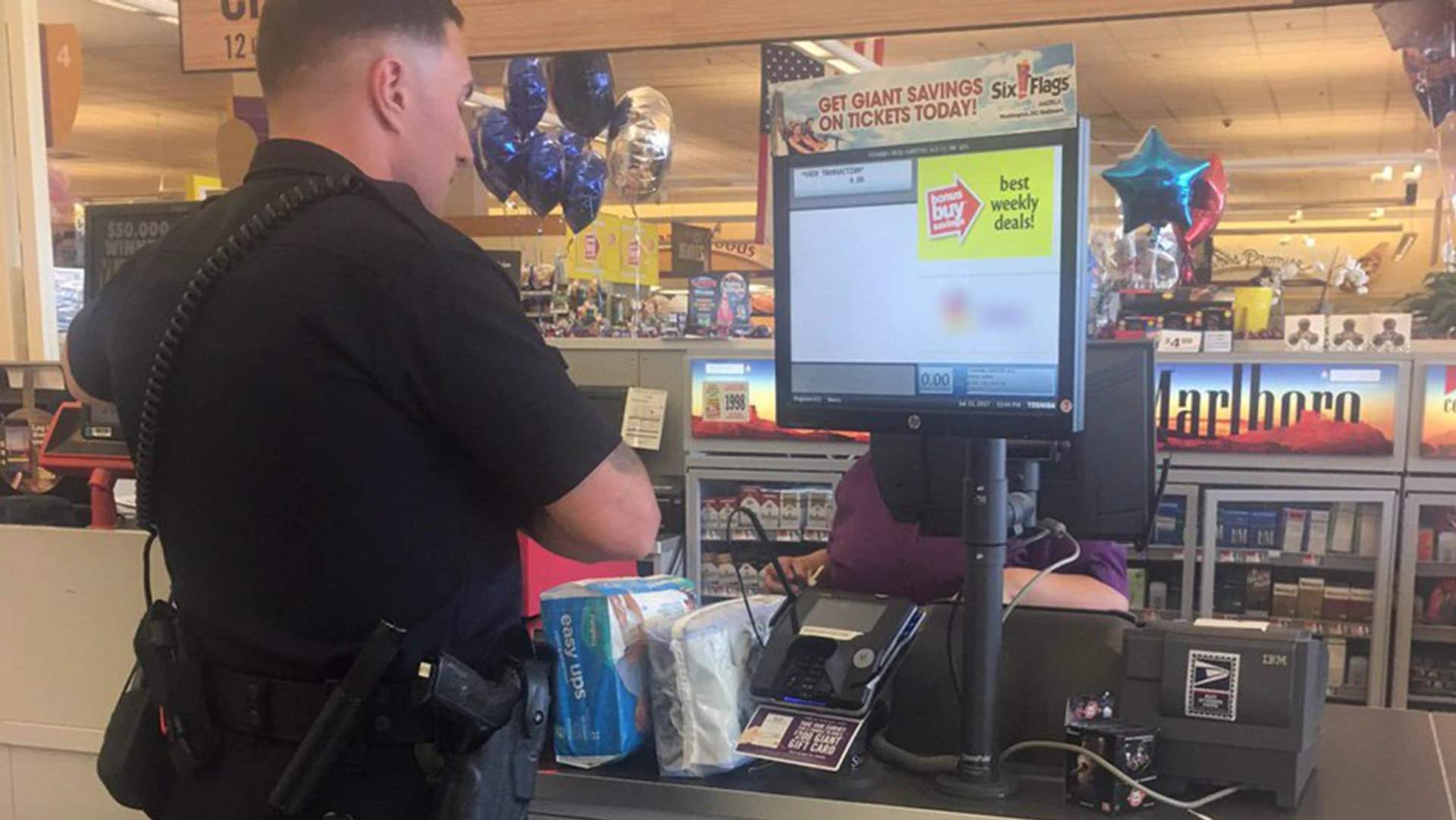 Police officer in uniform standing at a store checkout counter purchasing packages of diapers
