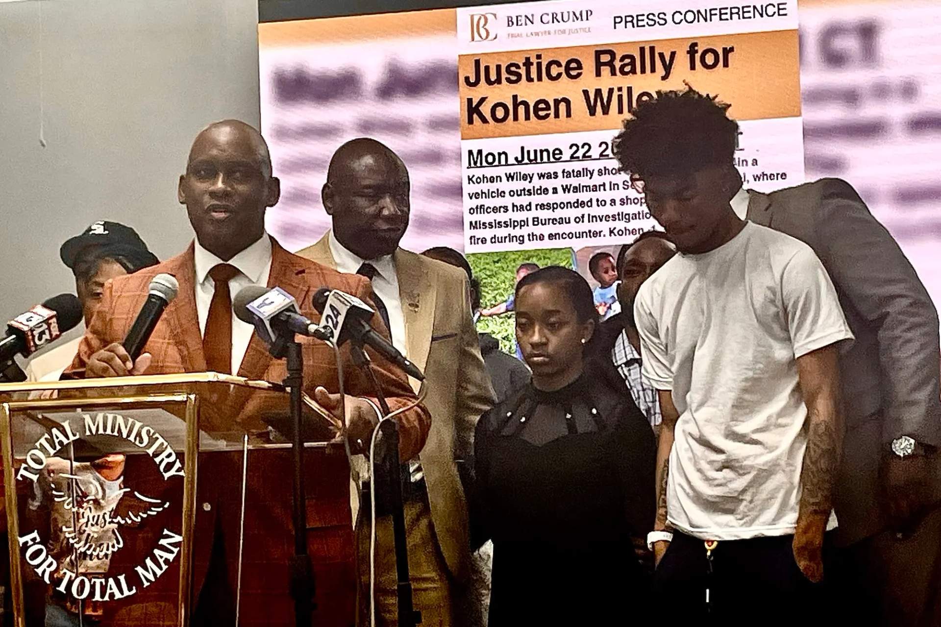 Vellesiya Wiley, a young Black woman in black clothing, stands with attorneys Ben Crump and Van Turner at outdoor microphones during a press conference in Senatobia, Mississippi
