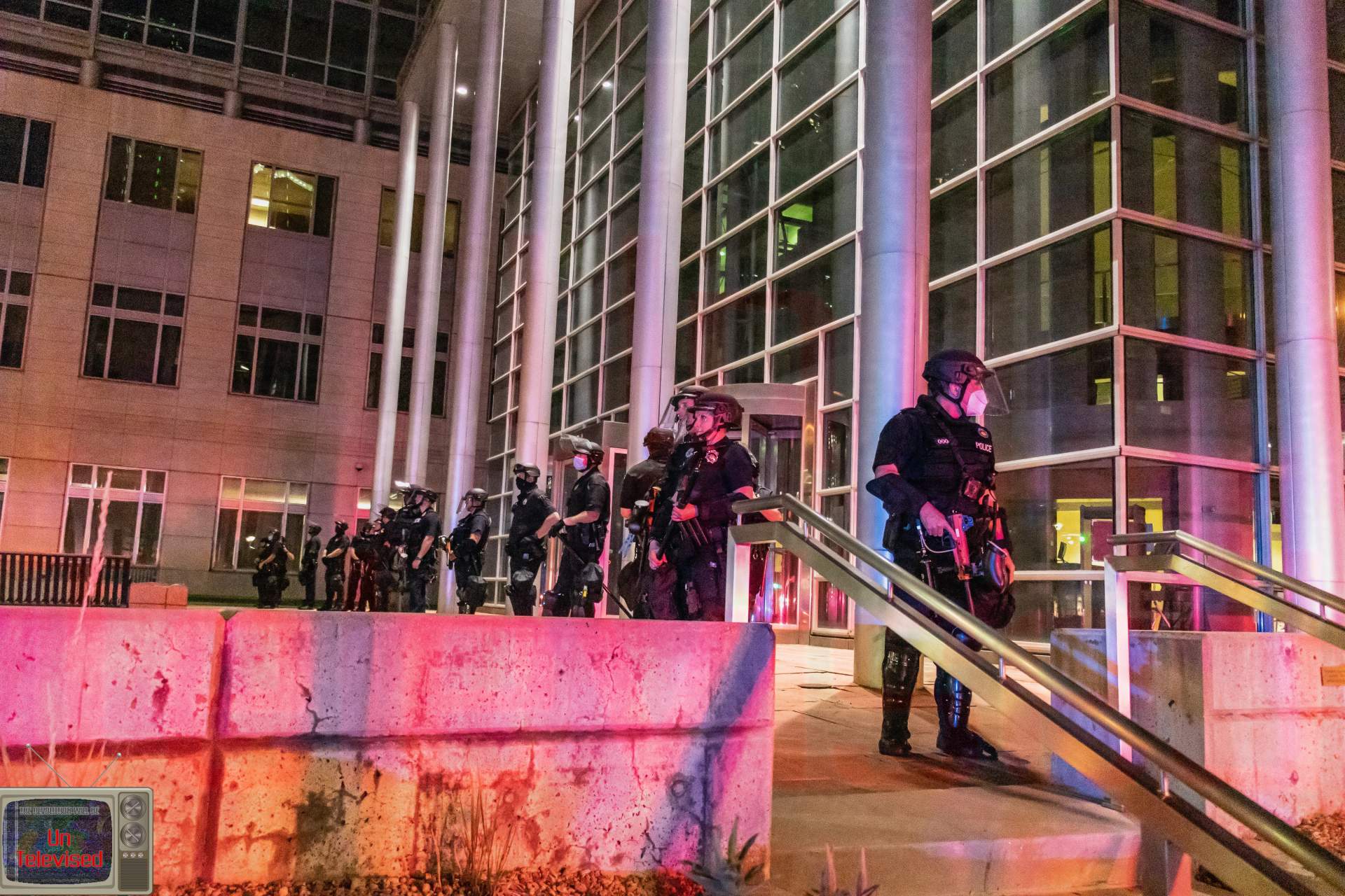  Riot-equipped police officers in helmets, masks, and tactical gear stand guard outside the federal courthouse. [Radical Edward - Untelevised Media]