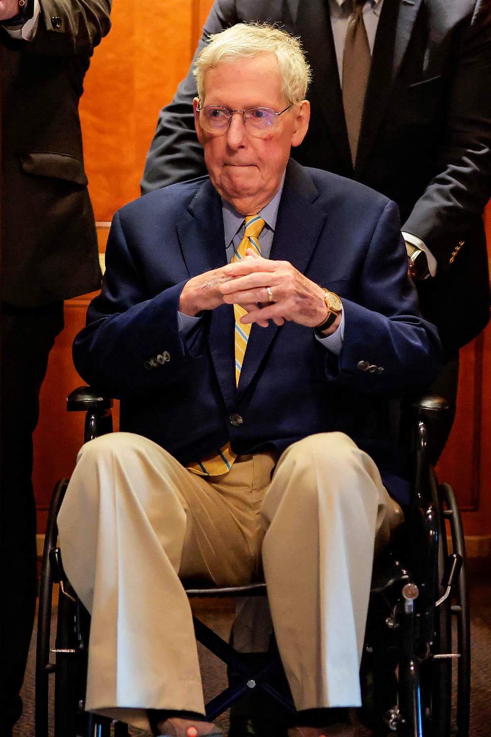 Mitch McConnell seated in a wheelchair being pushed through a hallway by staff members at the U.S. Capitol