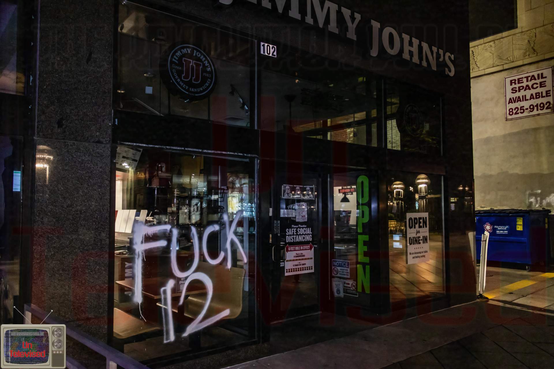 The Jimmy John's sandwich shop entrance, still open for dine-in, with "FUCK 12" spray-painted across the front window. [Radical Edward - Untelevised Media]