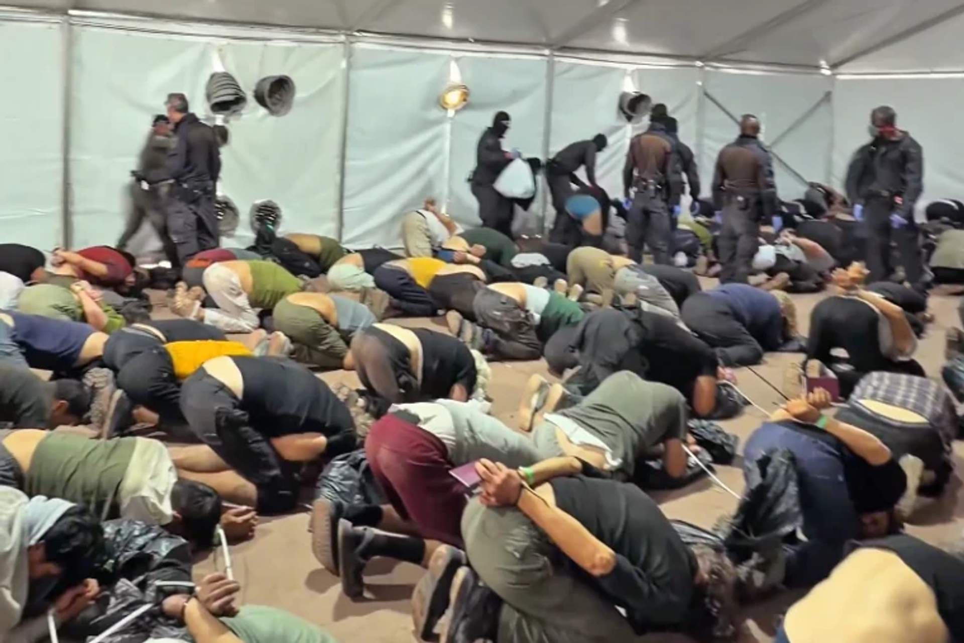 Dozens of detained activists kneeling on concrete floor with hands bound behind backs at a port facility