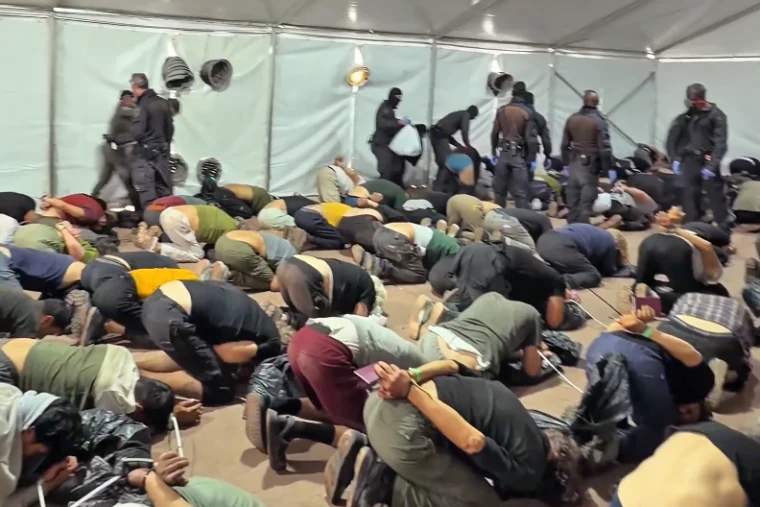 Dozens of detained activists kneeling on concrete floor with hands bound behind backs at a port facility