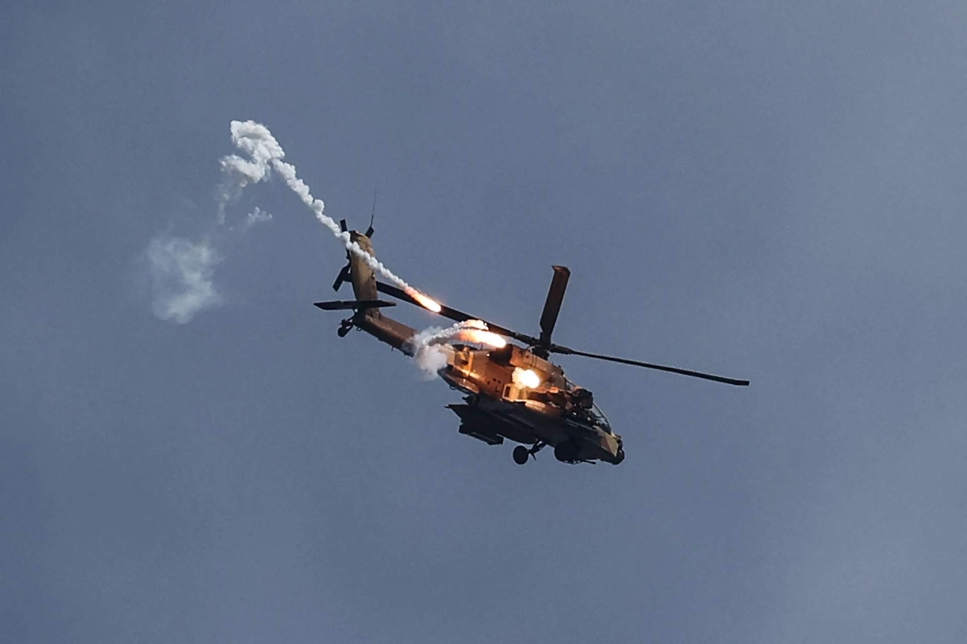 Israeli AH-64 Apache helicopter flying over open terrain near the Gaza border firing defensive flares