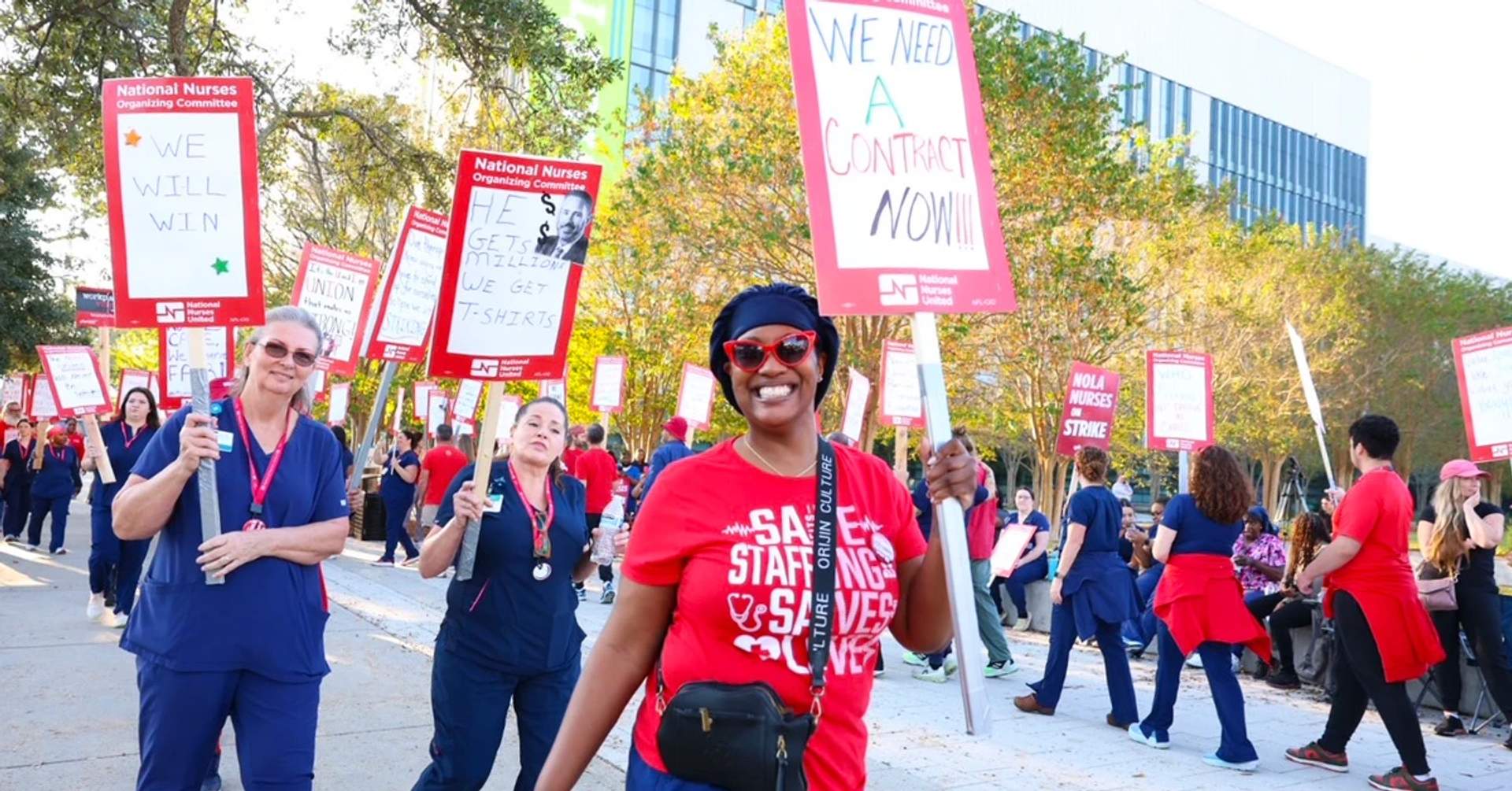 Nurses holding signs on a picket line outside University Medical Center in New Orleans during their sixth strike, one sign reads We Need a Contract NOW