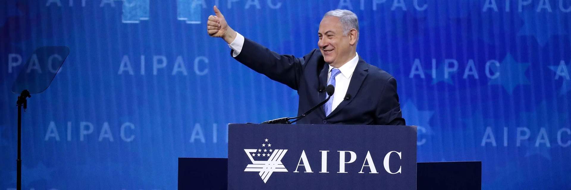 Benjamin Netanyahu speaking from a podium at the AIPAC policy conference before a large audience with Israeli and American flags on stage