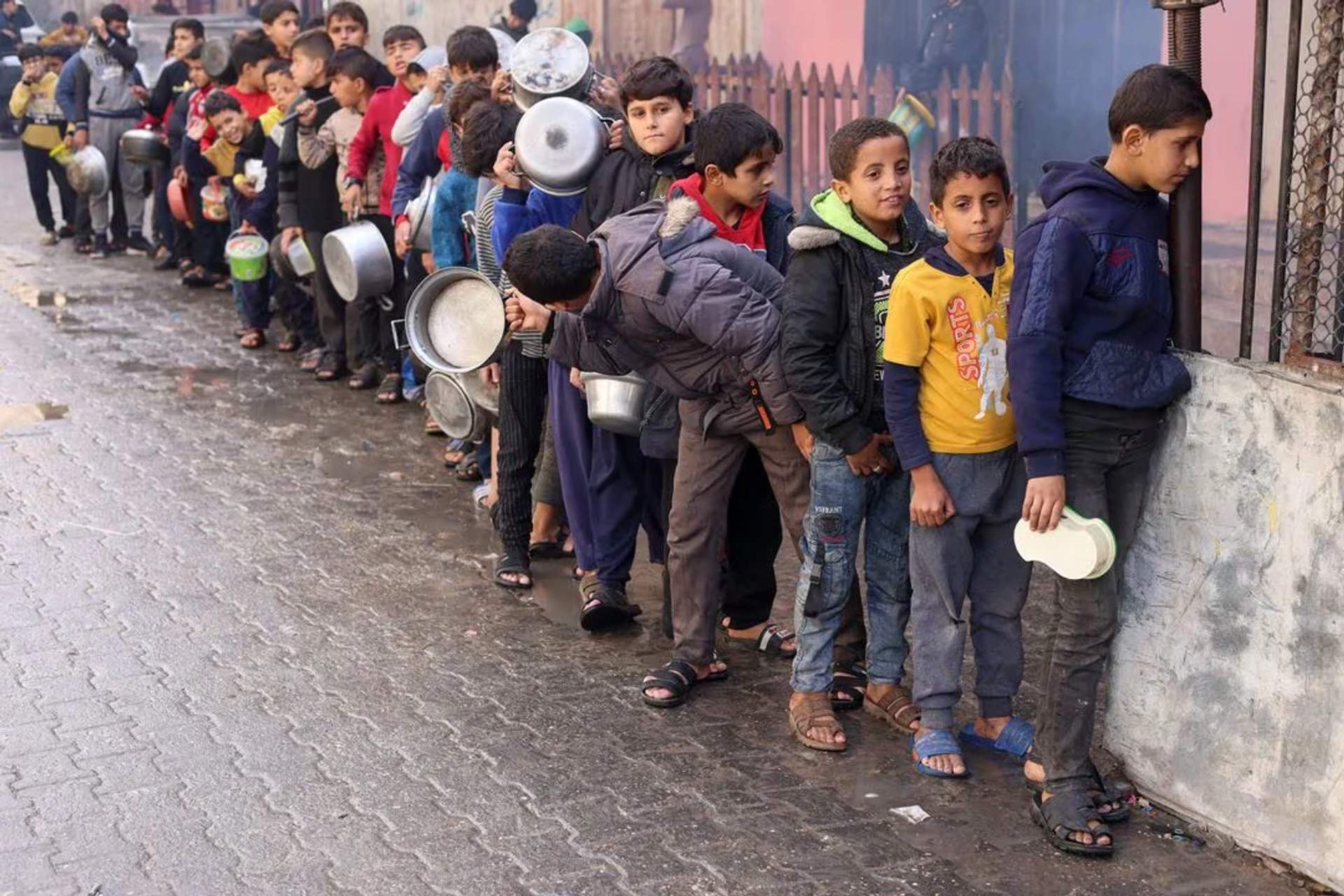 Palestinian children carry pots as they queue to receive food cooked by a charity kitchen, amid shortages in food supplies, in Rafah in the southern Gaza Strip on December 14, 2023.
