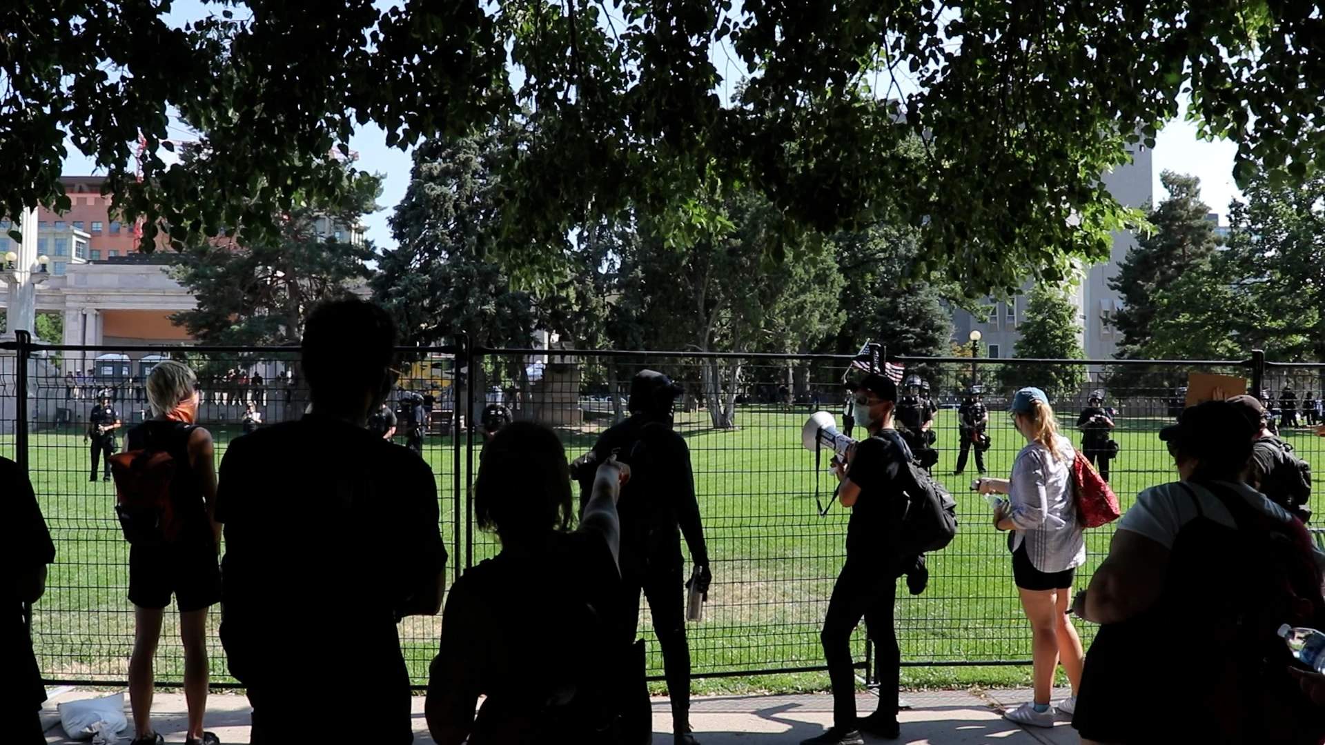 Protesters seek shade as they taunt riot police standing baking in the hot July sun.