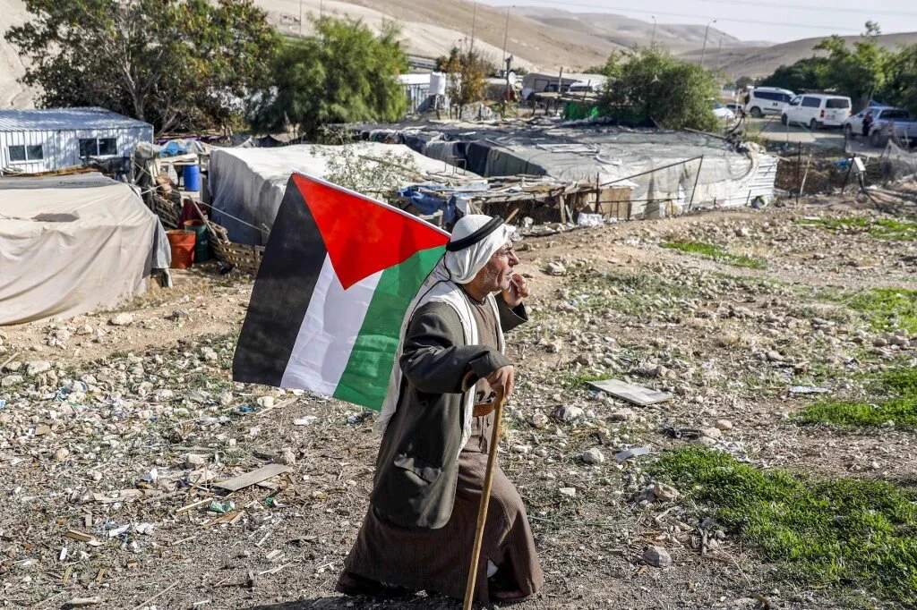 Palestinian man walking with flag through Khan al-Ahmar Bedouin village in the occupied West Bank
