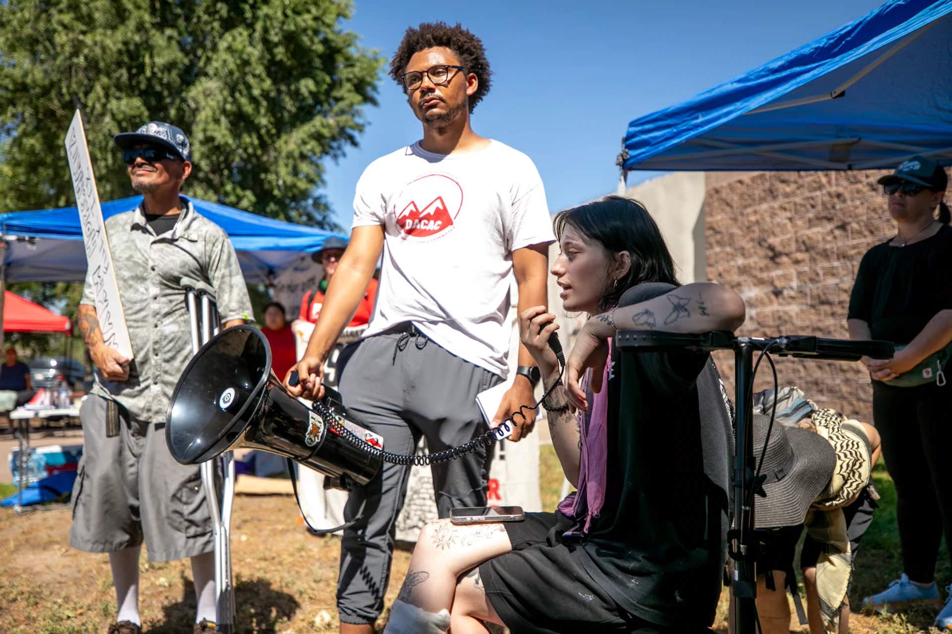 Emma Landis standing on crutches with bandaged leg speaking to supporters outside the Aurora ICE detention center