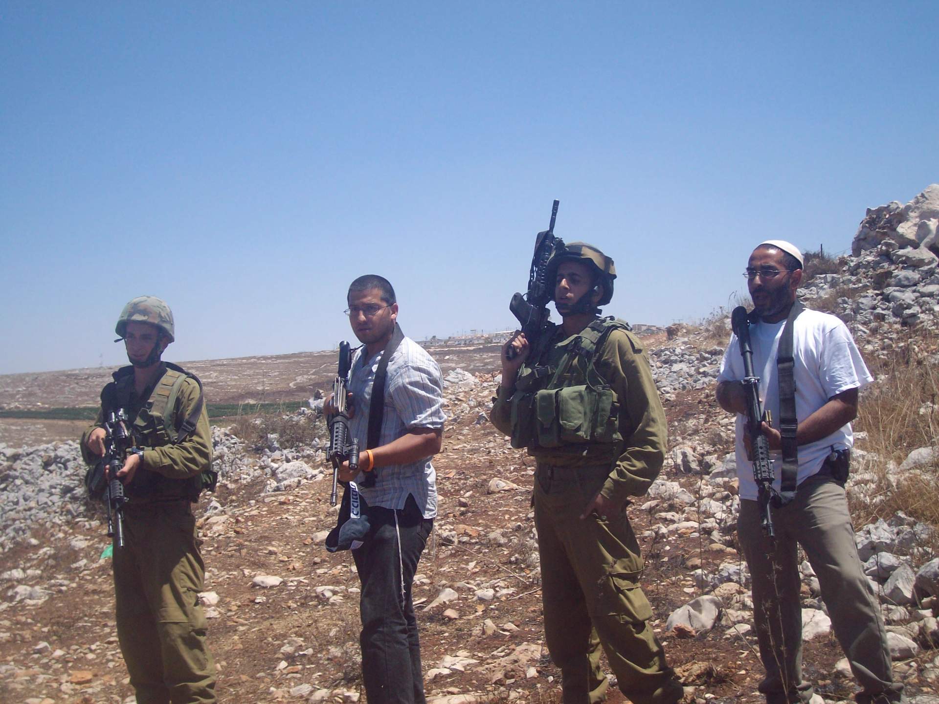 Israeli settlers and soldiers standing near a Palestinian village in the West Bank, August 2009