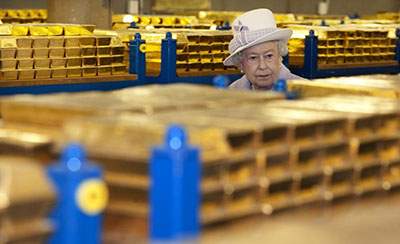 Queen Elizabeth II inspects rows of stacked gold bars during a visit to a bank vault.