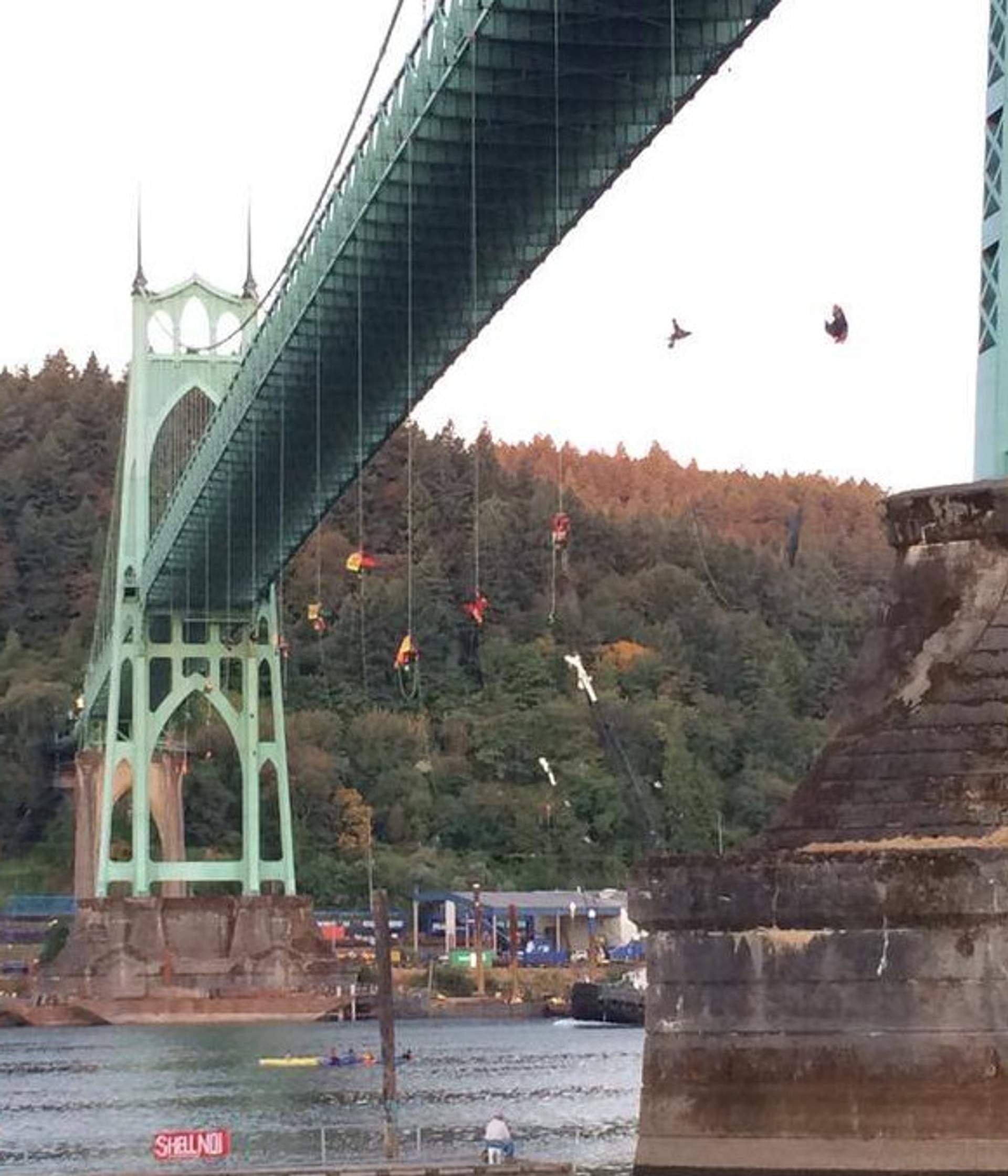 Activists rappel from the St. Johns Bridge, suspended above the water on ropes hung with red and yellow banners.