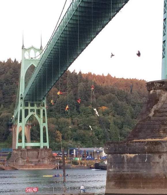Activists rappel from the St. Johns Bridge, suspended above the water on ropes hung with red and yellow banners.