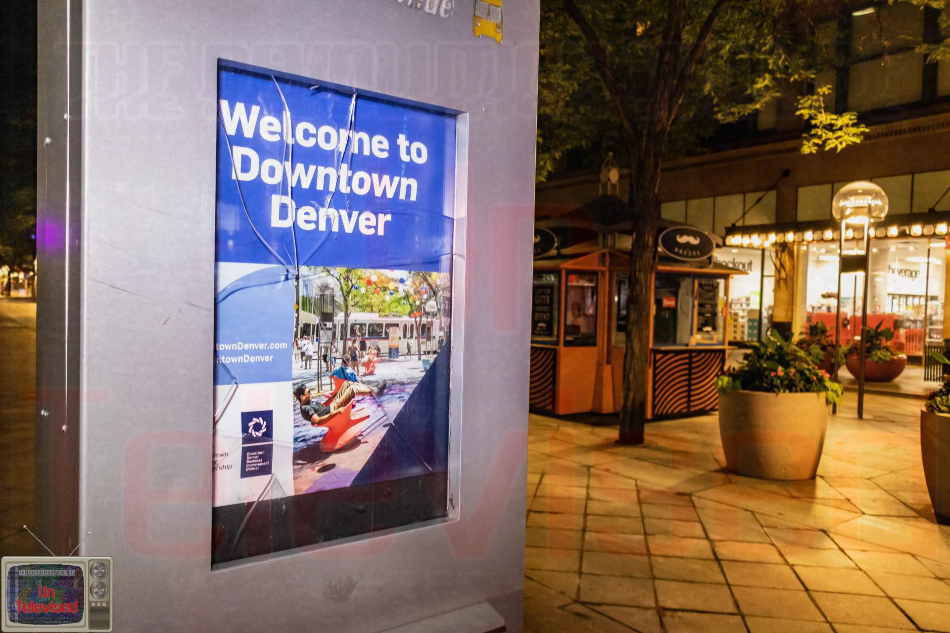 A cracked "Welcome to Downtown Denver" informational sign/kiosk on the mall, with shops visible in the background.  [Radical Edward - Untelevised Media]