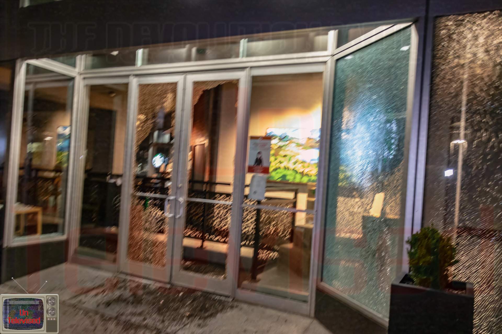 A storefront entrance with cracked and shattered glass panels along the doors and windows.  [Radical Edward - Untelevised Media]