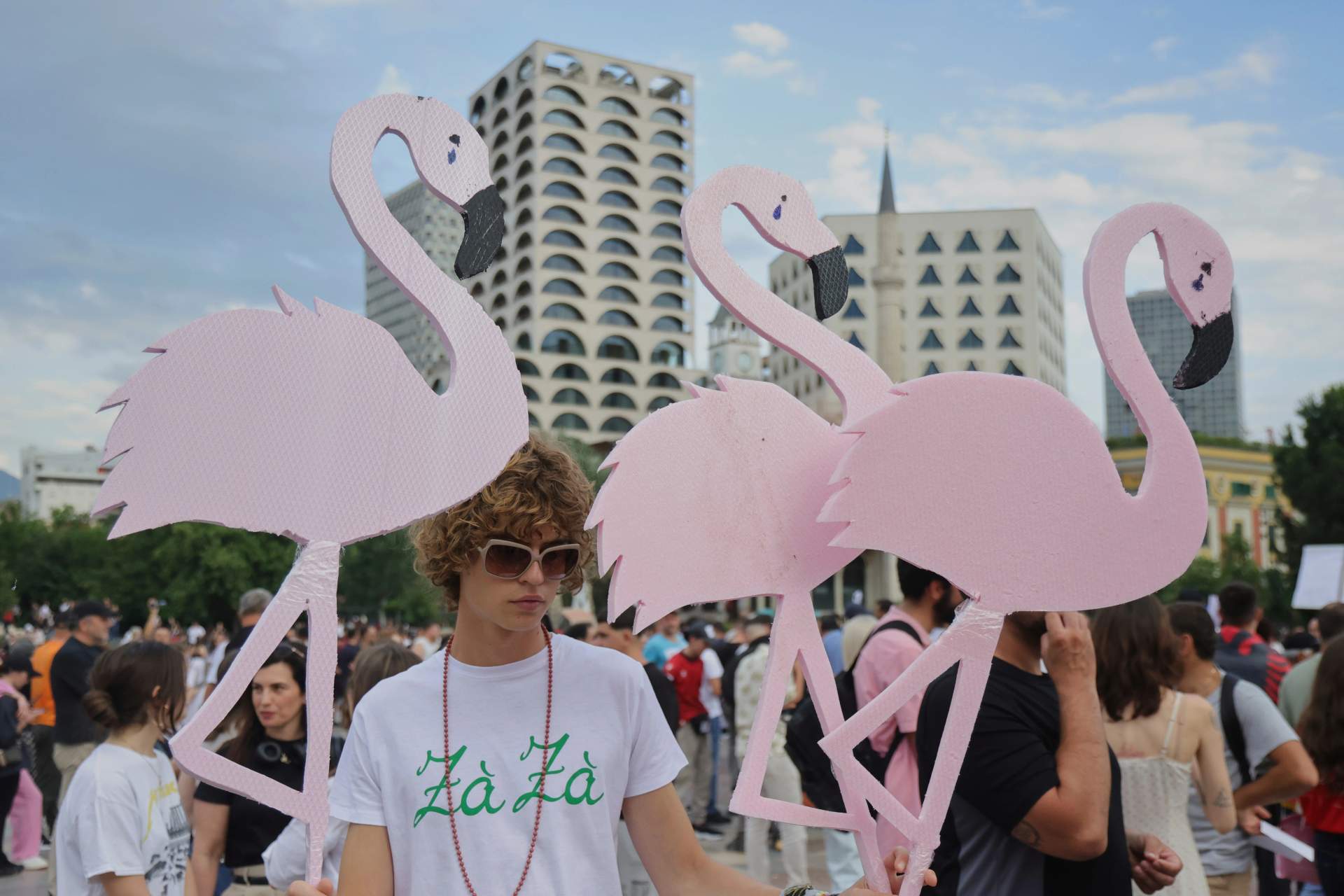 Thousands of protesters crowd a street in Tirana holding pink flamingo cutouts above their heads in protest against a Kushner-linked resort development