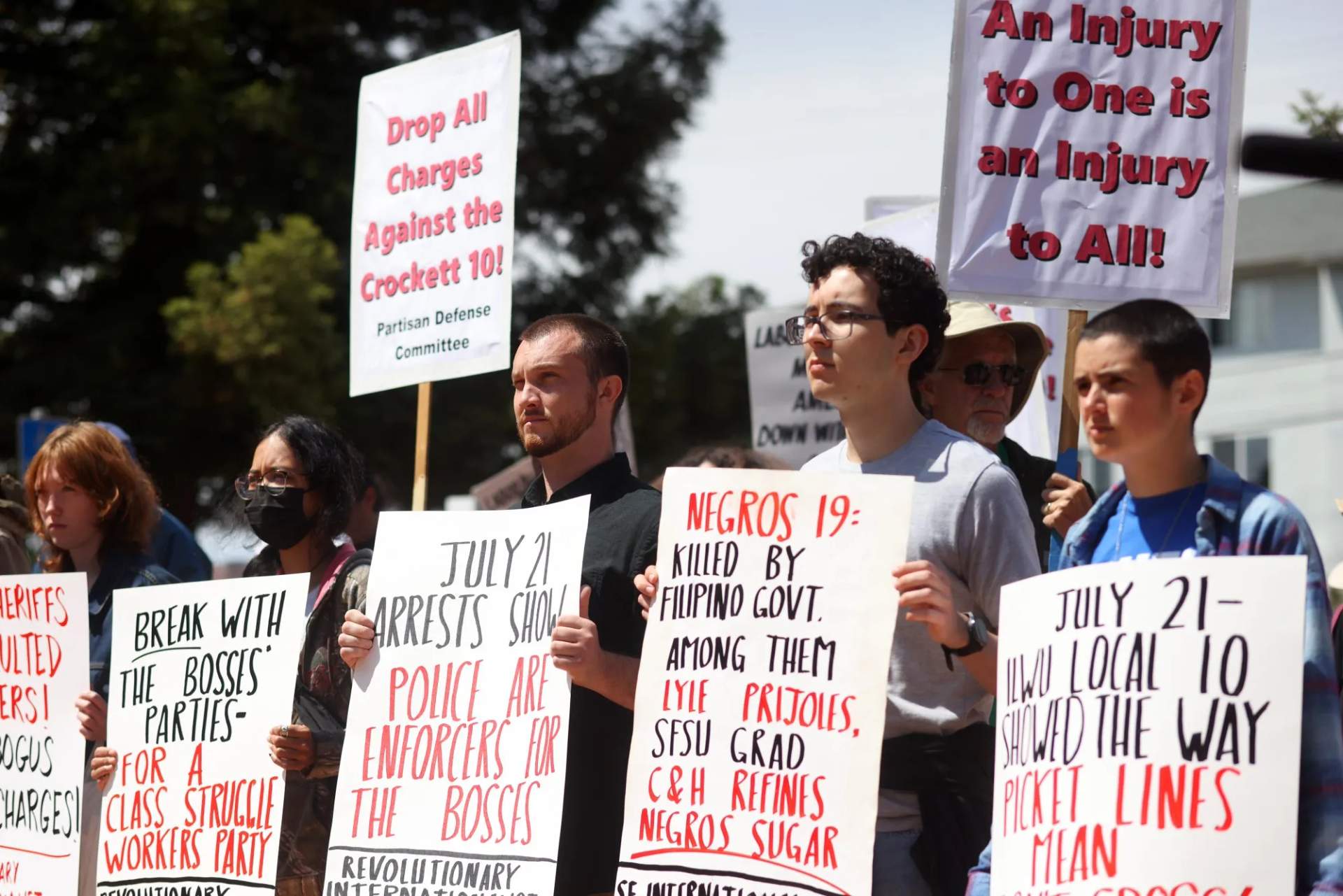 A crowd of supporters gathers in a courthouse courtyard holding signs and union flags during a rally for the Crockett 10 in Richmond, California