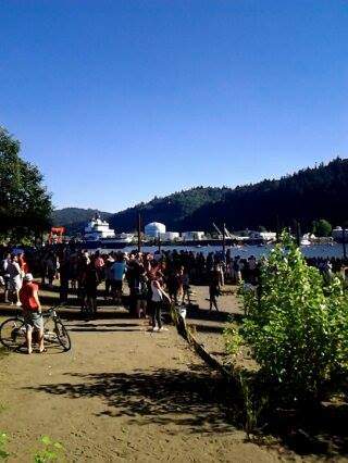 A crowd gathers along the riverbank with the Fennica visible on the water in the distance.