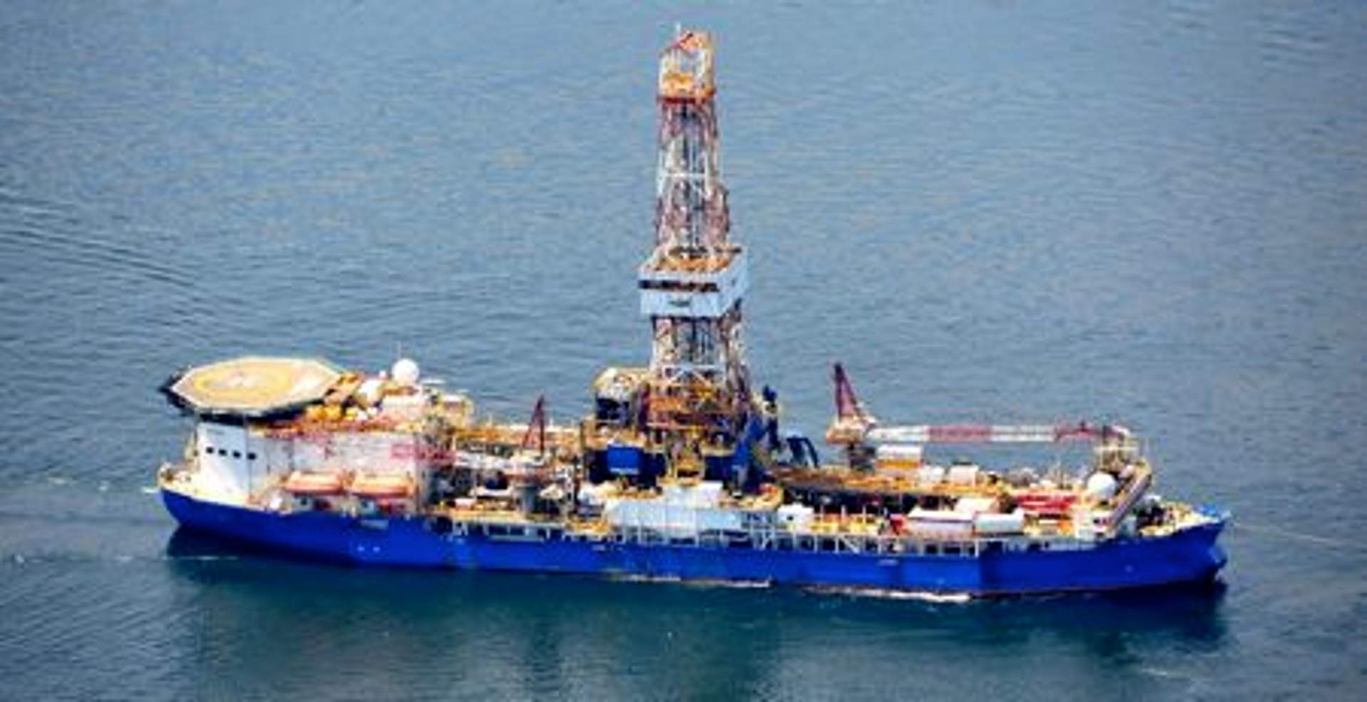 The Noble Discoverer, a large blue-and-white drillship, at sea.