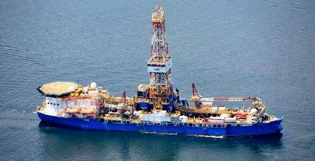 The Noble Discoverer, a large blue-and-white drillship, at sea.