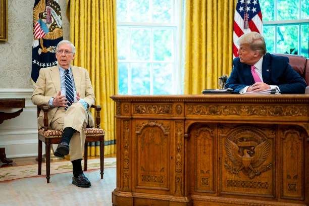 Mitch McConnell seated and listening as Donald Trump speaks at a meeting with other officials present