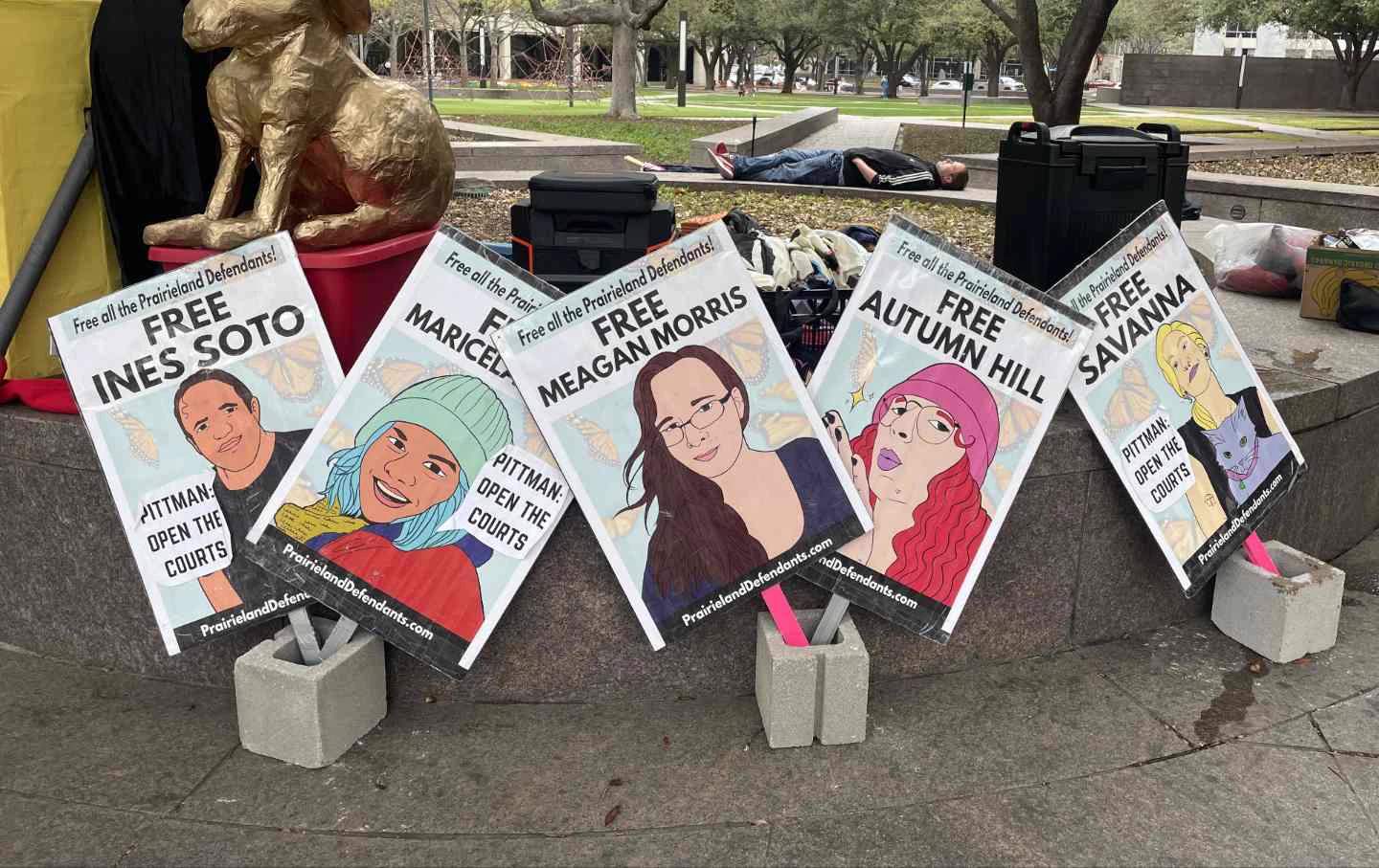 Multiple hand-made posters and signs attached to a fence outside a federal courthouse with messages supporting the Prairieland defendants