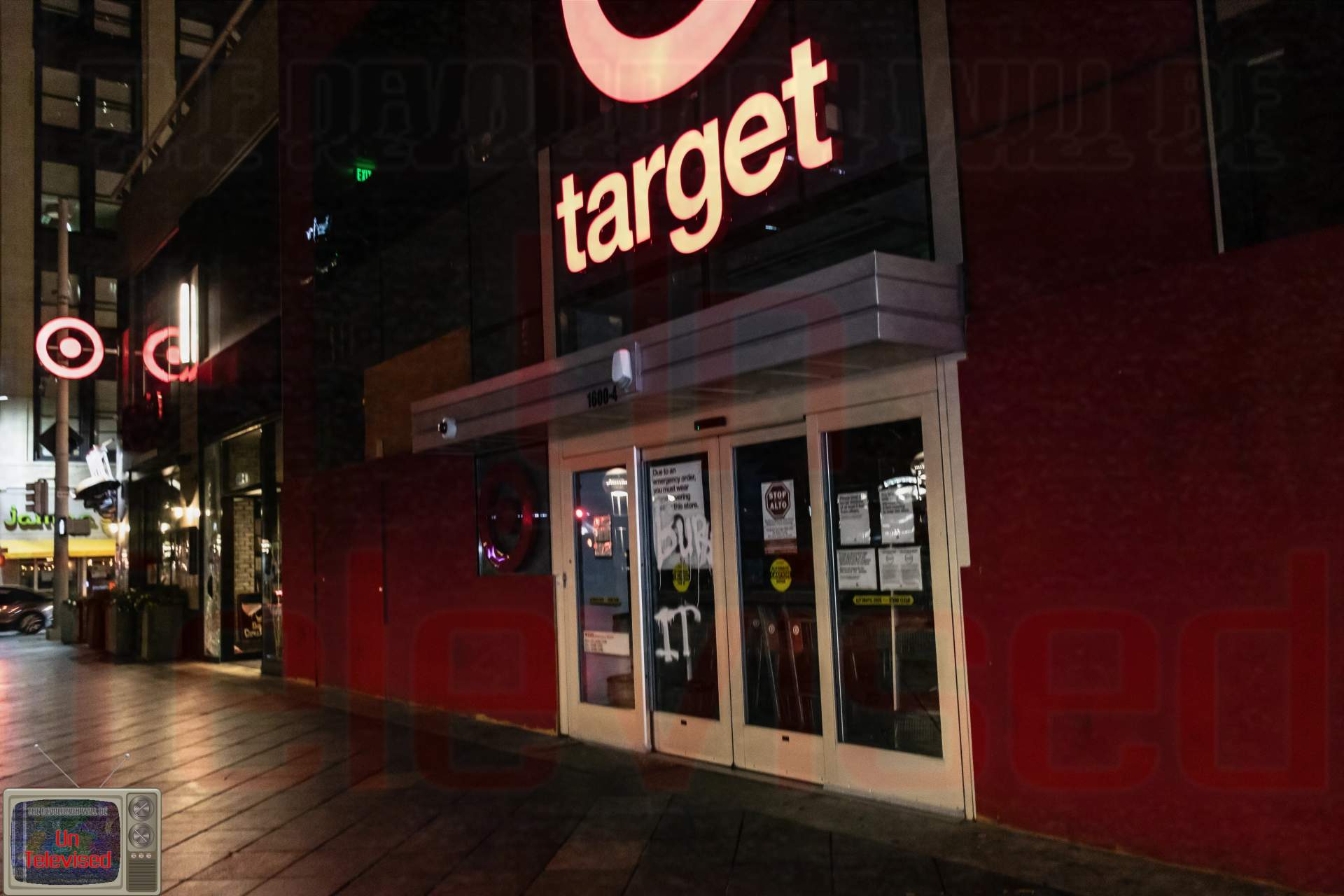 A wider view of the Target storefront entrance at night, showing the same "BURN IT" graffiti on the doors beneath the glowing Target sign. [Radical Edward - Untelevised Media]