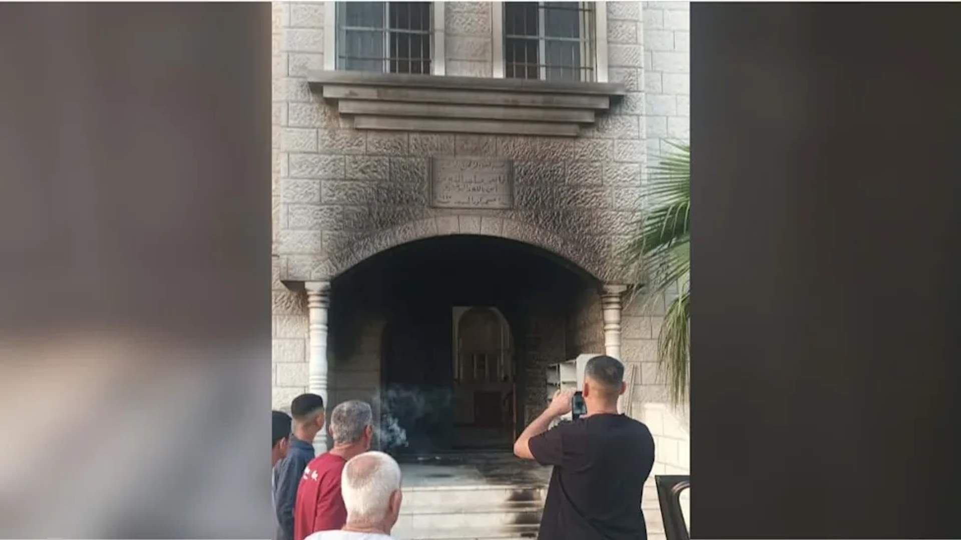Palestinian men standing outside a mosque with visible fire damage
