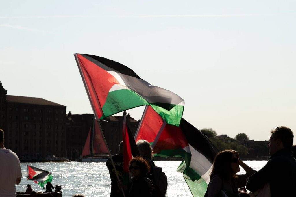 Flotilla departing for Gaza with supporters waving flags on shore.