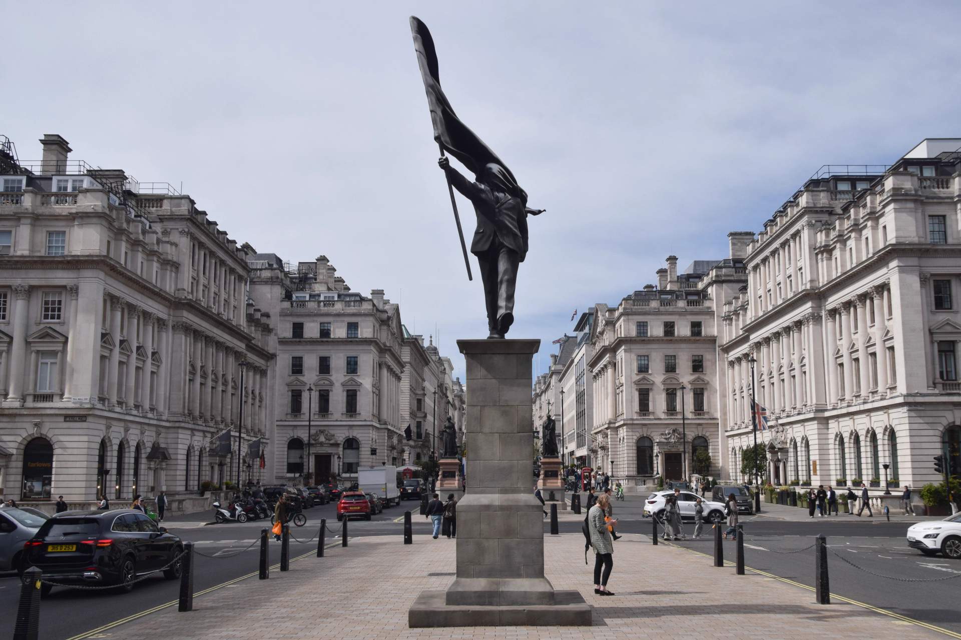 Suited figure holds a large flag that completely obscures his face, shown walking forward with one foot suspended over the edge of the stone plinth