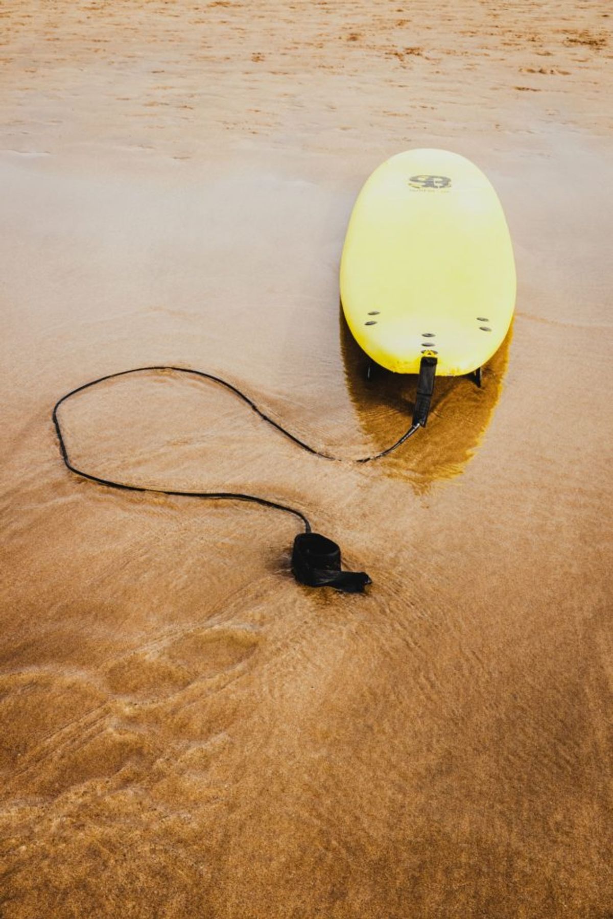 A yellow beginner's surfboard in the sand