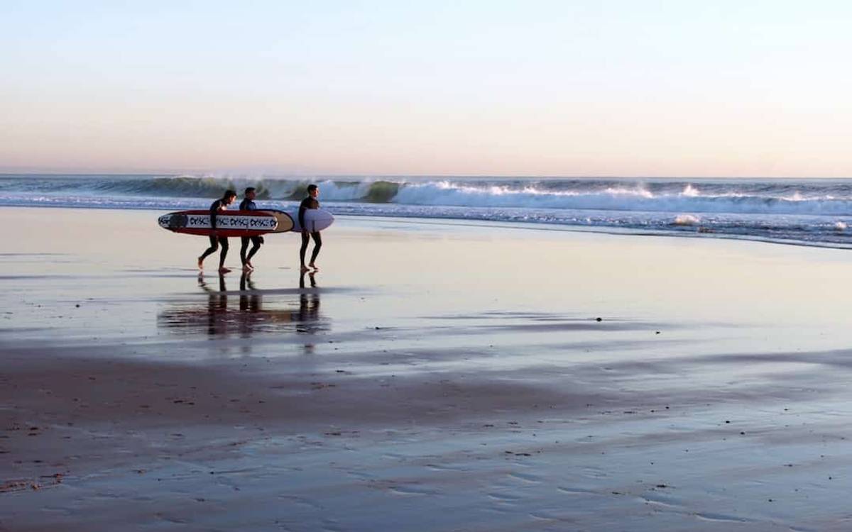 Three surfers with longboards on the beach in Carcavelos