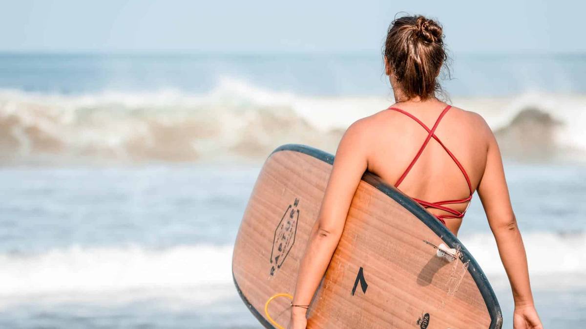 a surfer entering the sea holding a rapture surfcamps surfboard
