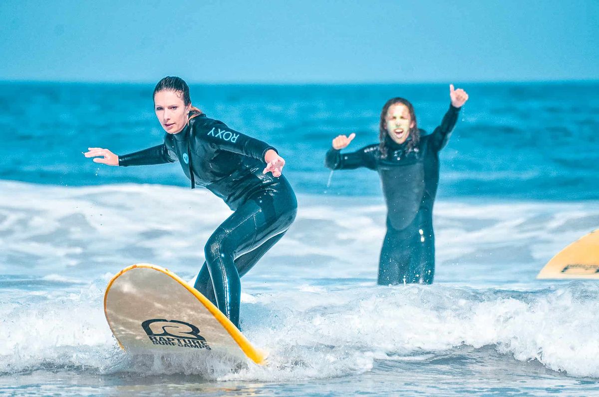 A girl surfing while another person cheers her from behind.